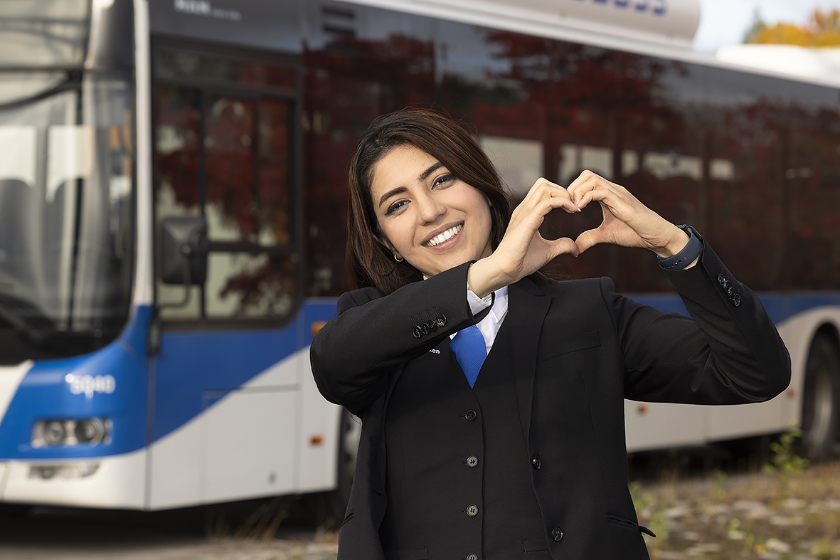 Kvinnlig bussförare som håller händer som ett hjärta framför en buss